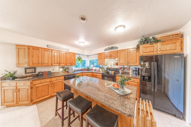 145 Deer Run Ln, Layton, UT 84040 - kitchen featuring black appliances, a textured ceiling, a breakfast bar, a kitchen island, and stone counters
