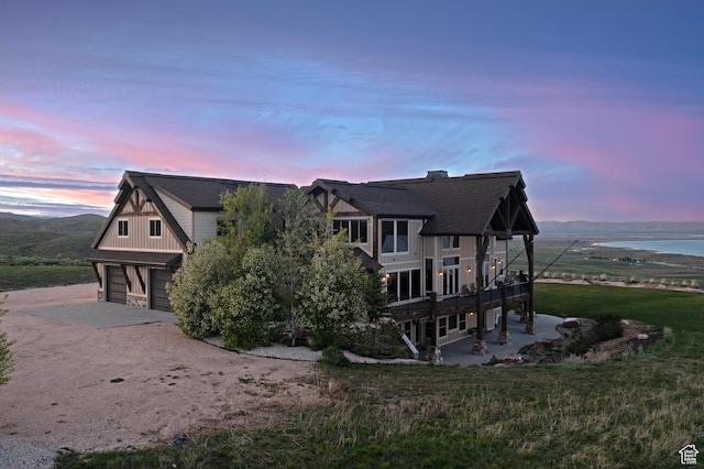 1560 Reserve Dr, Fish Haven, ID 83287 - property exterior at dusk with an attached garage, driveway, a water view, board and batten siding, and a yard