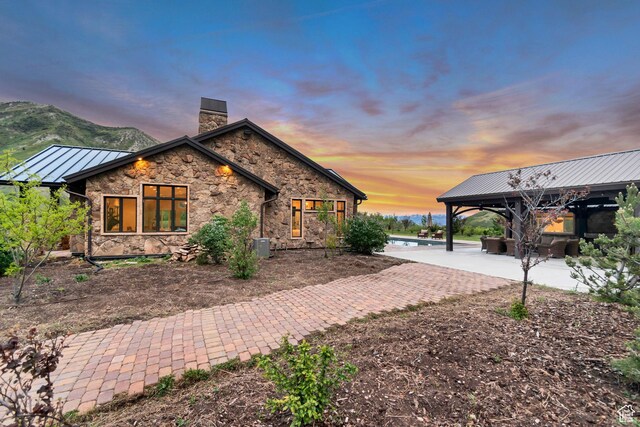 370 S Got Teeth Ln E, Emigration Canyon, UT 84108 - property exterior at dusk with a chimney, stone siding, a gazebo, a standing seam roof, and a patio area