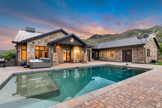 370 S Got Teeth Ln E, Emigration Canyon, UT 84108 - back of house at dusk with a standing seam roof, a hot tub, stone siding, a patio, and a metal roof