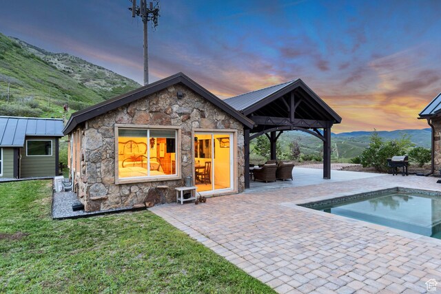 370 S Got Teeth Ln E, Emigration Canyon, UT 84108 - back of house at dusk with stone siding, a patio area, a mountain view, an outdoor pool, and a metal roof