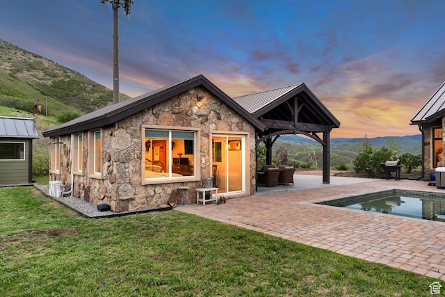 370 S Got Teeth Ln E, Emigration Canyon, UT 84108 - back of house at dusk with stone siding, a patio, a lawn, and a standing seam roof