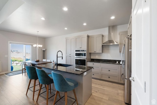 1308 E Daffodil Ct Unit 150, Layton, UT 84040 - kitchen featuring wall chimney range hood, appliances with stainless steel finishes, light wood-style flooring, a center island with sink, and a kitchen breakfast bar