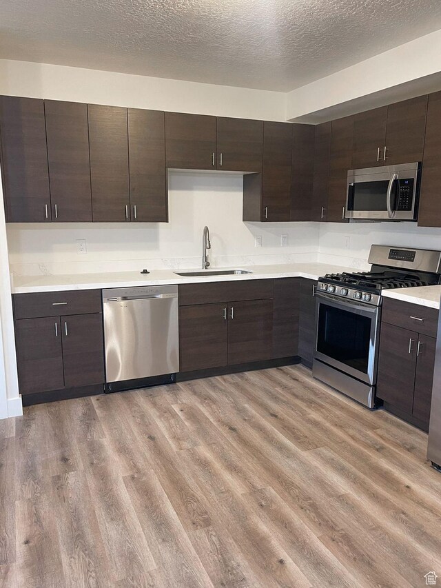 113 N 1400 E, Pleasant Grove, UT 84062 - kitchen with appliances with stainless steel finishes, light wood-style floors, dark brown cabinetry, light countertops, and a textured ceiling