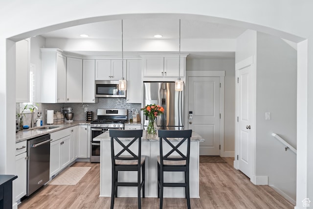 10401 S Liffey Ln, South Jordan, UT 84009 - kitchen with appliances with stainless steel finishes, arched walkways, light wood-type flooring, decorative backsplash, and a kitchen island