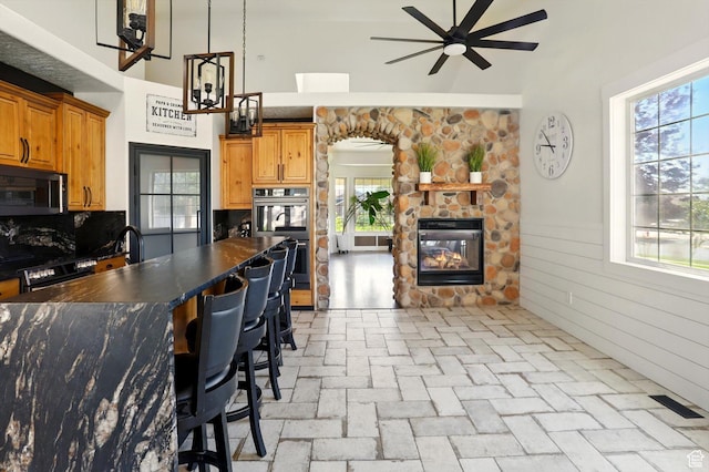 7414 S Regal Dr, West Jordan, UT 84081 - kitchen with dark countertops, a ceiling fan, double oven, a stone fireplace, and brick flooring