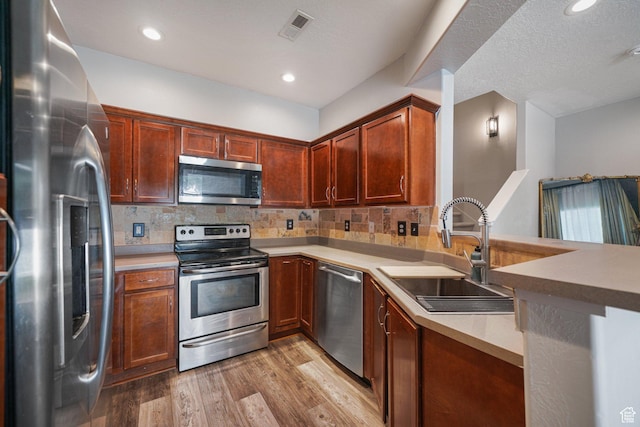 211 Greenfield Cir Unit 119, Heber City, UT 84032 - kitchen featuring appliances with stainless steel finishes, light wood finished floors, decorative backsplash, light countertops, and a peninsula