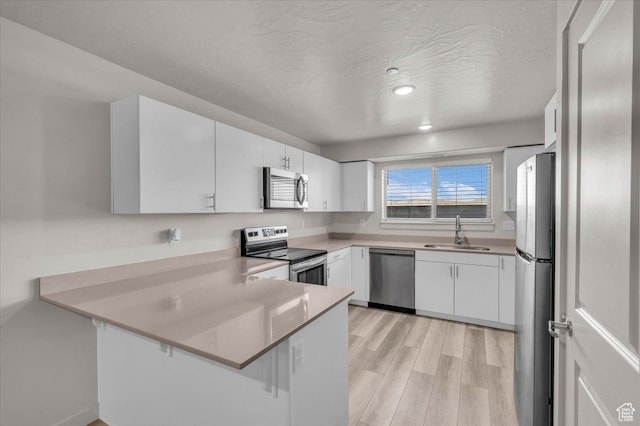 1167 E Telegraph St # A104, Washington, UT 84780 - kitchen with appliances with stainless steel finishes, a peninsula, white cabinets, light wood-type flooring, and a textured ceiling