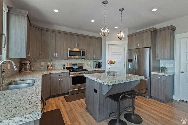 735 W Horizon Dr, Lehi, UT 84043 - kitchen with appliances with stainless steel finishes, a kitchen island, decorative backsplash, light wood-style floors, and a kitchen bar