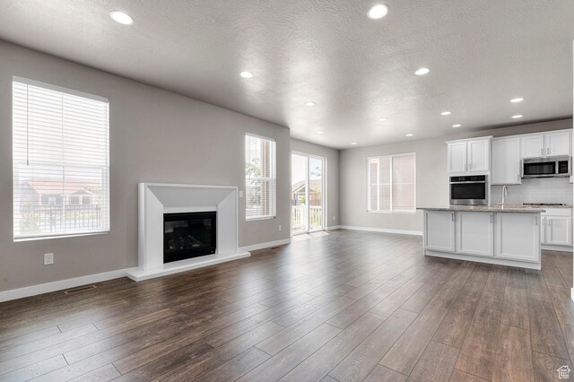 1298 E Salt Creek Peak, Eagle Mountain, UT 84005 - unfurnished living room featuring a textured ceiling, dark wood-style flooring, recessed lighting, and a glass covered fireplace