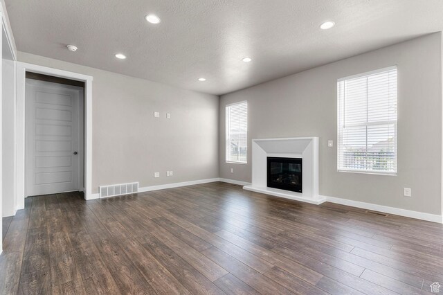 1298 E Salt Creek Peak, Eagle Mountain, UT 84005 - unfurnished living room featuring healthy amount of natural light, a textured ceiling, dark wood-type flooring, a glass covered fireplace, and recessed lighting