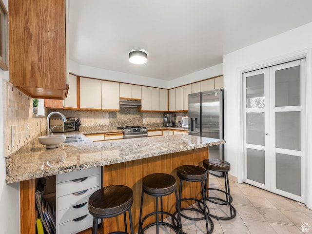 1705 E Plata Way, Sandy, UT 84093 - kitchen featuring appliances with stainless steel finishes, under cabinet range hood, a peninsula, decorative backsplash, and light stone countertops