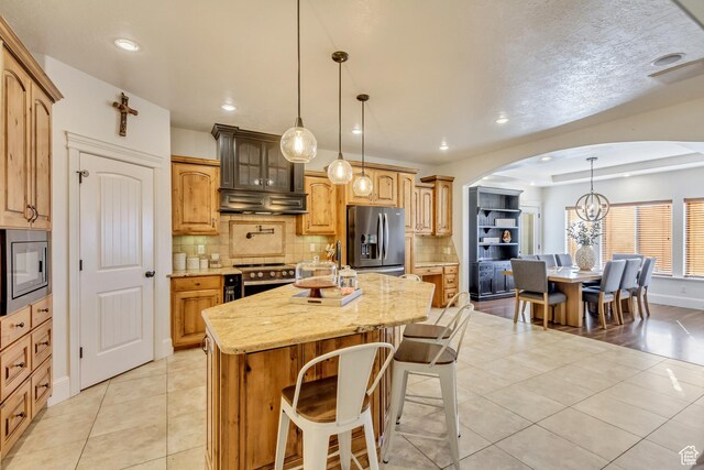 338 S Holdaway Rd, Vineyard, UT 84059 - kitchen featuring appliances with stainless steel finishes, arched walkways, a kitchen island, light tile patterned floors, and decorative backsplash