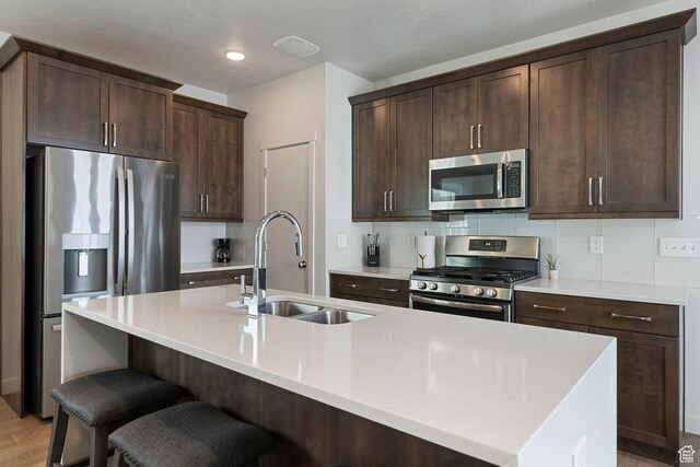 6691 Woods Rose Dr Unit 45, Park City, UT 84098 - kitchen with appliances with stainless steel finishes, dark brown cabinetry, an island with sink, backsplash, and a kitchen bar