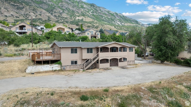 9096 N Canyon Rd, Cedar Hills, UT 84062 - view of front of house featuring stucco siding, stone siding, stairway, a deck with mountain view, and dirt driveway