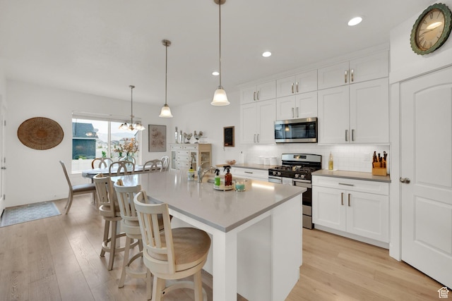 4655 N Ibapah St, Eagle Mountain, UT 84005 - kitchen with stainless steel appliances, light wood-style flooring, tasteful backsplash, white cabinetry, and a kitchen bar