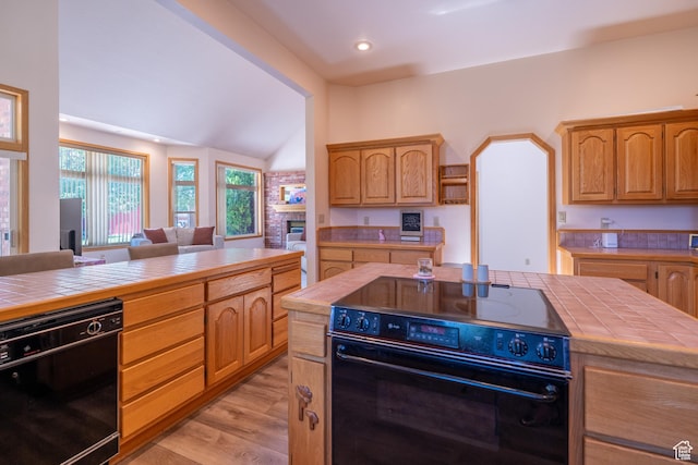 4163 S Beeman Rd, Moab, UT 84532 - kitchen featuring black appliances, tile countertops, lofted ceiling, light wood-type flooring, and a fireplace