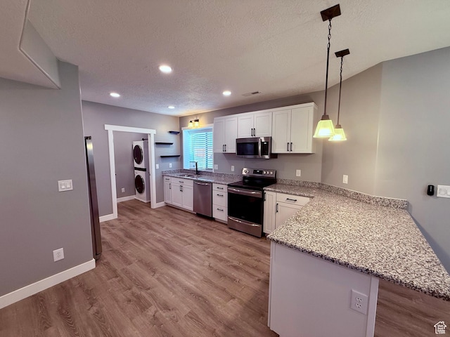 12887 S Wild Mare Way, Riverton, UT 84096 - kitchen with appliances with stainless steel finishes, estacked washer and dryer, a peninsula, white cabinetry, and a textured ceiling