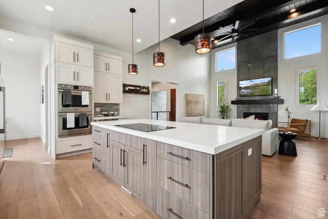 8960 Parleys Ln, Park City, UT 84098 - kitchen featuring double oven, a large fireplace, black electric cooktop, light wood finished floors, and a towering ceiling