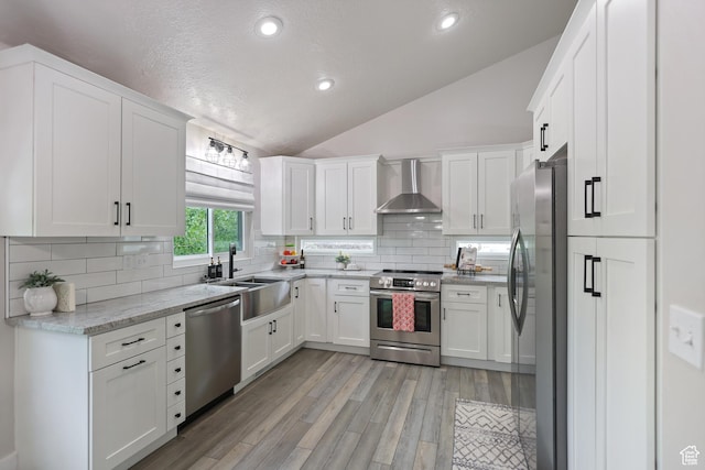 10787 S Pine Shadow Rd, South Jordan, UT 84009 - kitchen featuring appliances with stainless steel finishes, wall chimney range hood, vaulted ceiling, white cabinetry, and light wood-style floors
