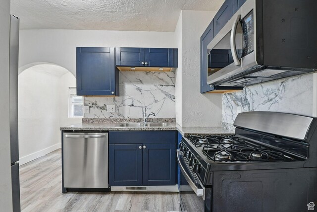 2973 Adams Ave, Ogden, UT 84403 - kitchen with stainless steel appliances, blue cabinets, light wood-type flooring, tasteful backsplash, and arched walkways