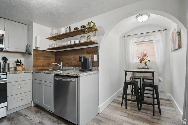 2973 Adams Ave, Ogden, UT 84403 - kitchen featuring stainless steel dishwasher, light wood finished floors, arched walkways, light stone countertops, and a textured ceiling