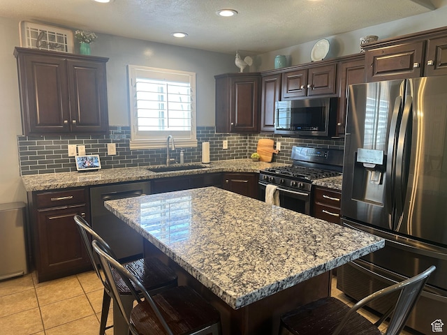 1295 S 4050 W, Syracuse, UT 84075 - kitchen with stainless steel appliances, a breakfast bar area, dark brown cabinets, decorative backsplash, and light stone counters