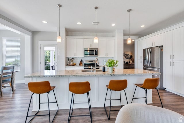 10616 S Wistful Way S, Jordan, UT 84009 - kitchen featuring appliances with stainless steel finishes, tasteful backsplash, white cabinetry, a breakfast bar, and an island with sink