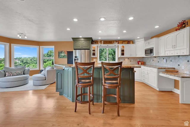 1269 Alice Ln, Farmington, UT 84025 - kitchen featuring stainless steel appliances, light wood finished floors, a breakfast bar, a textured ceiling, and white cabinets