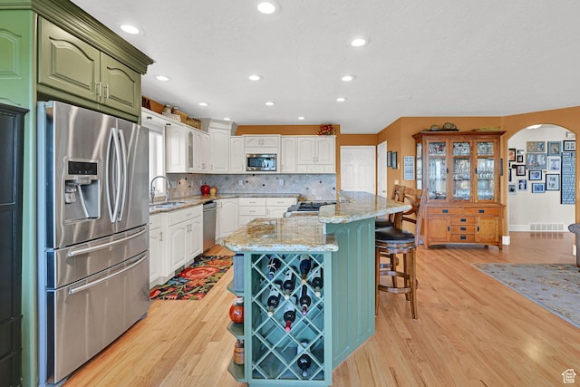 1269 Alice Ln, Farmington, UT 84025 - kitchen featuring appliances with stainless steel finishes, arched walkways, light wood-style flooring, green cabinets, and a kitchen breakfast bar