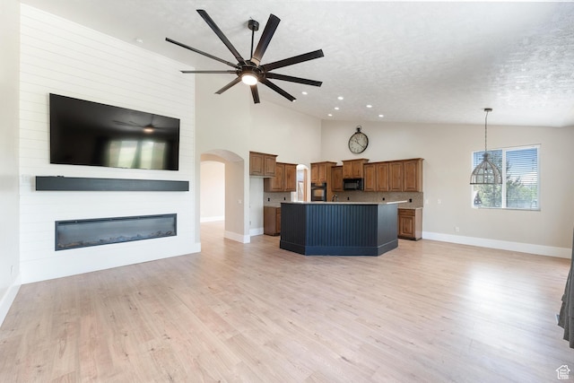 8743 N Franklin Dr E, Eagle Mountain, UT 84005 - unfurnished living room with arched walkways, a ceiling fan, a textured ceiling, a large fireplace, and light wood-style floors