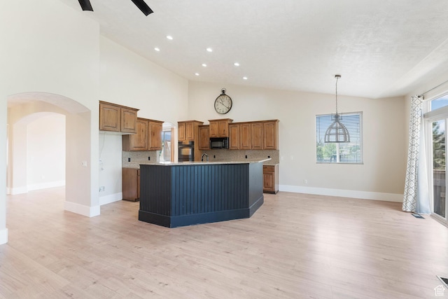 8743 N Franklin Dr E, Eagle Mountain, UT 84005 - kitchen with black appliances, brown cabinetry, an island with sink, arched walkways, and light wood-style flooring