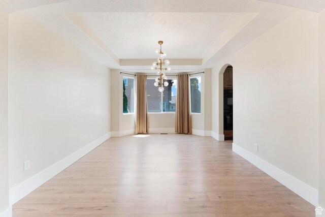 8743 N Franklin Dr E, Eagle Mountain, UT 84005 - unfurnished dining area with arched walkways, a tray ceiling, a chandelier, and light wood-style flooring