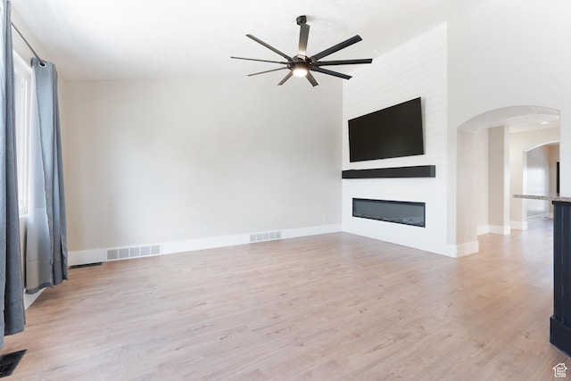 8743 N Franklin Dr E, Eagle Mountain, UT 84005 - unfurnished living room featuring a ceiling fan, arched walkways, light wood-style flooring, and a fireplace