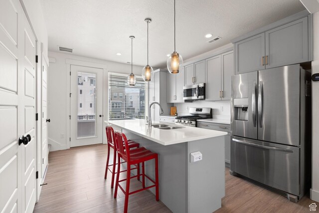 11079 S Lake Run Rd, South Jordan, UT 84009 - kitchen with stainless steel appliances, gray cabinetry, wood finished floors, a kitchen island with sink, and a breakfast bar