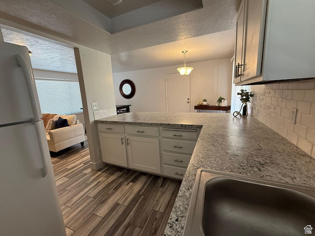 5509 S 2150 W, Roy, UT 84067 - kitchen featuring freestanding refrigerator, a peninsula, decorative backsplash, dark wood-style flooring, and a textured ceiling