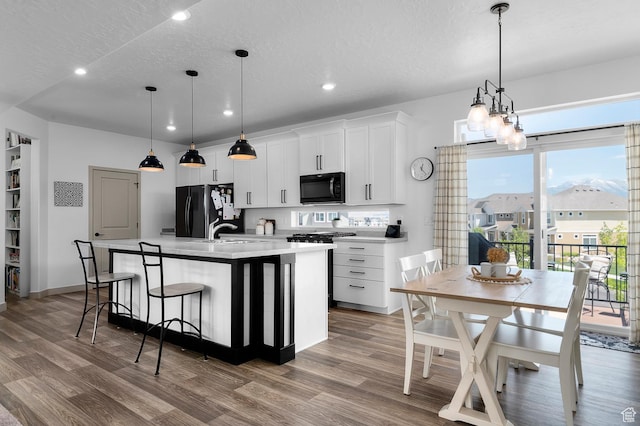 106 E Polaris Dr, Saratoga Springs, UT 84045 - kitchen featuring black appliances, recessed lighting, wood finished floors, a center island with sink, and white cabinets