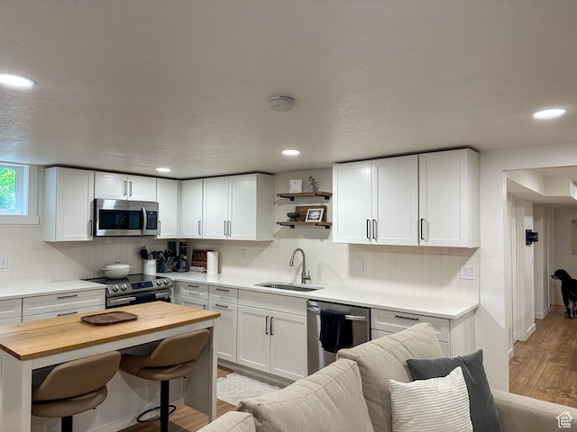 3269 Liberty Ave, Ogden, UT 84403 - kitchen with appliances with stainless steel finishes, wooden counters, a breakfast bar, light wood-style floors, and white cabinetry