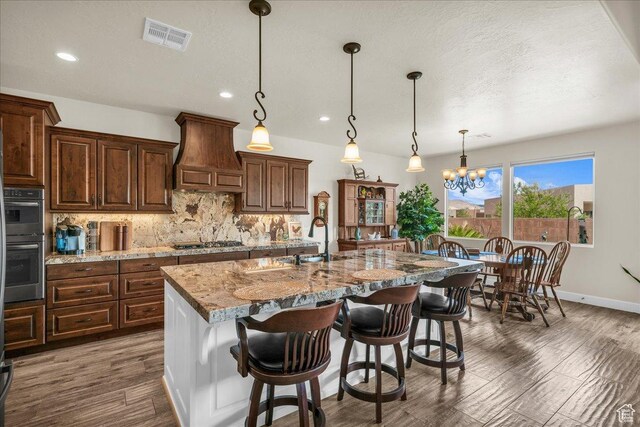 1472 W Pocket Mesa Dr, St George, UT 84770 - kitchen with custom exhaust hood, stainless steel appliances, tasteful backsplash, light stone countertops, and an island with sink
