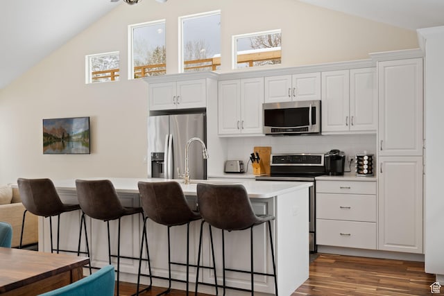 3569 E Avondale Dr S, Cottonwood Heights, UT 84121 - kitchen with stainless steel appliances, a kitchen island with sink, a breakfast bar area, white cabinetry, and high vaulted ceiling