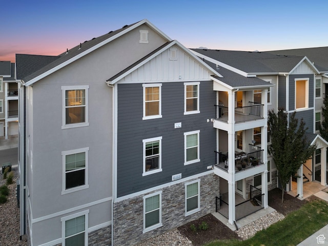 14654 S Bloom Dr W Unit K301, Herriman, UT 84096 - back of property at dusk featuring stone siding, a balcony, board and batten siding, and stucco siding