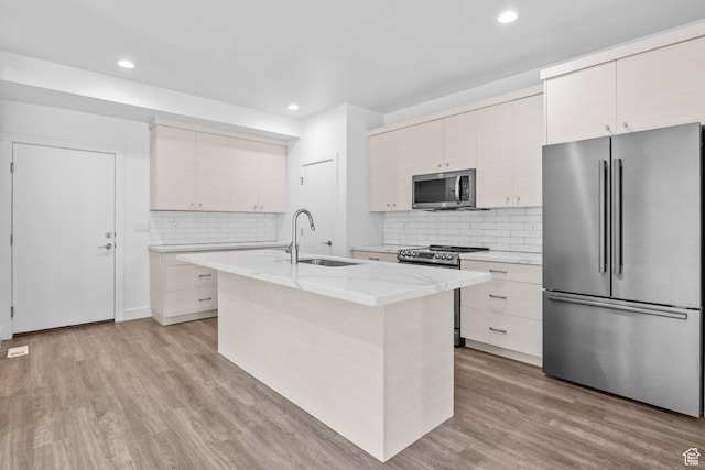 1046 W Albion Meadow Way, Bluffdale, UT 84065 - kitchen with stainless steel appliances, decorative backsplash, light stone countertops, light wood-style floors, and a center island with sink