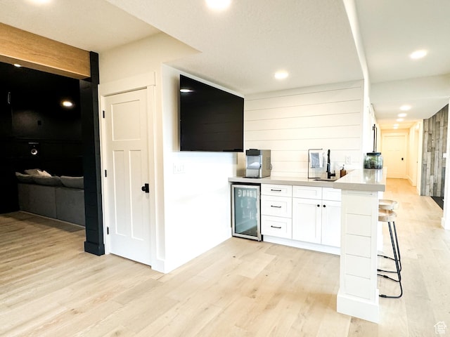 5469 N Meadow Lark Ln, Lehi, UT 84043 - kitchen with wine cooler, white cabinetry, light wood-style floors, light countertops, and a breakfast bar