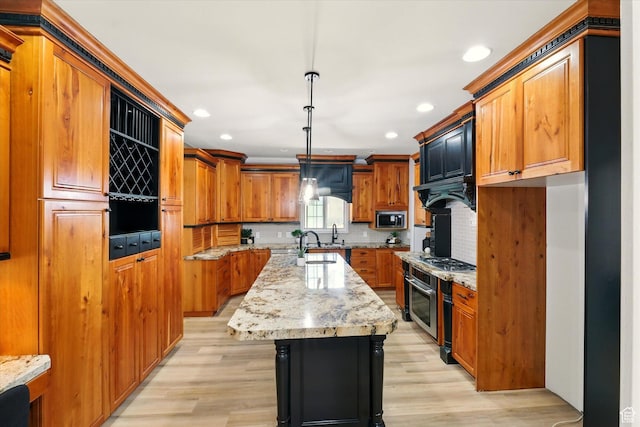 1655 W 2200 S, College Ward, UT 84339 - kitchen featuring stainless steel appliances, a kitchen island with sink, brown cabinetry, light wood finished floors, and backsplash