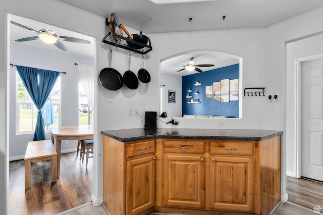 1738 N Brett St, Tooele, UT 84074 - kitchen featuring ceiling fan, arched walkways, wood finished floors, brown cabinetry, and dark stone countertops