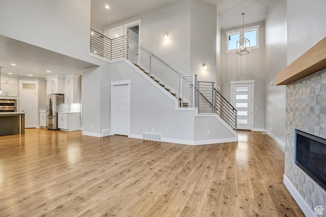 2508 E Lone Hill Dr, Draper Ut Cnty, UT 84020 - unfurnished living room with a high ceiling, stairs, light wood-style flooring, a glass covered fireplace, and recessed lighting