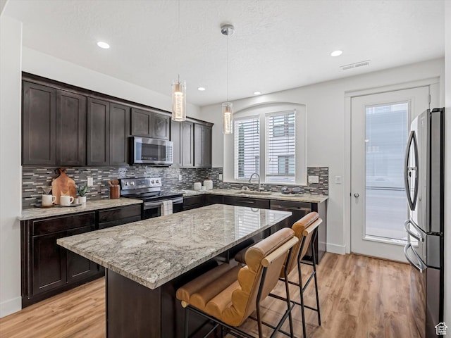 4851 W Daybreak Pkwy, South Jordan, UT 84009 - kitchen featuring appliances with stainless steel finishes, tasteful backsplash, a kitchen bar, light wood-style floors, and recessed lighting