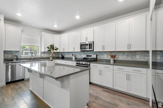 7335 N Harvest Crop Dr, Eagle Mountain, UT 84005 - kitchen featuring stainless steel appliances, light wood finished floors, white cabinets, a kitchen island, and backsplash