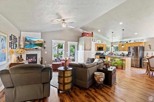793 E 2025 N, North Ogden, UT 84414 - living area featuring light wood-style flooring, a ceiling fan, vaulted ceiling, a textured ceiling, and a stone fireplace
