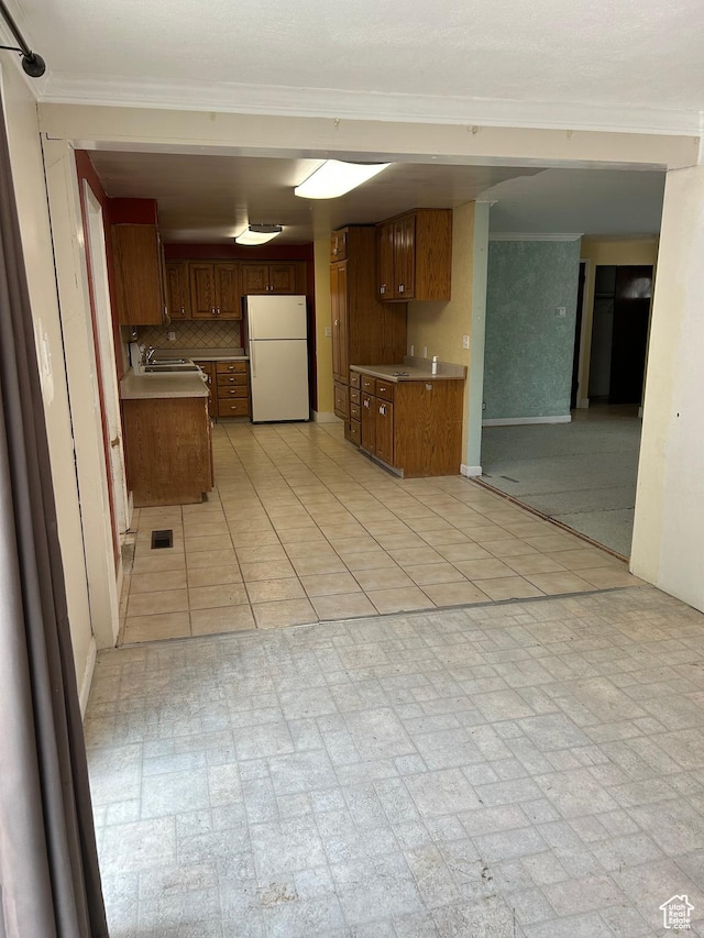 2784 W 2890 S, West Valley City, UT 84119 - kitchen featuring freestanding refrigerator, crown molding, brown cabinets, light countertops, and backsplash